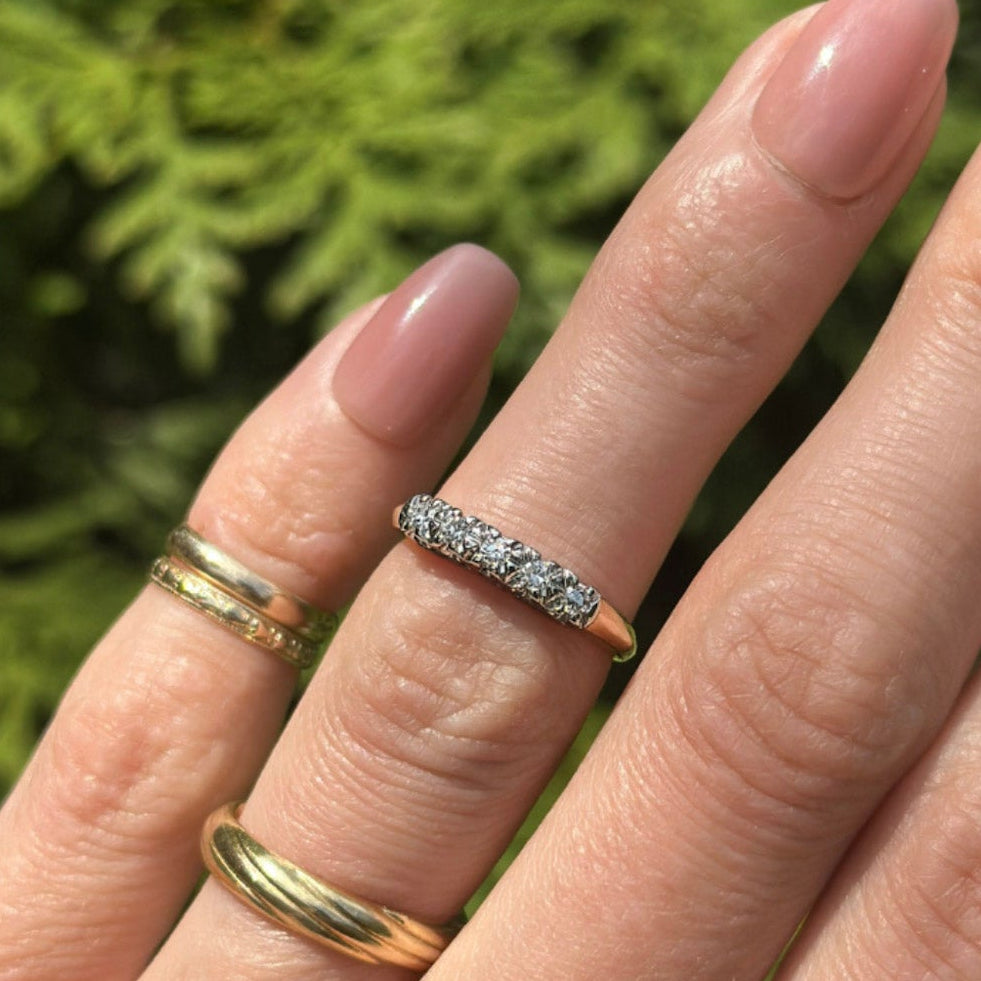 Hand wearing two gold rings with a blurred green background