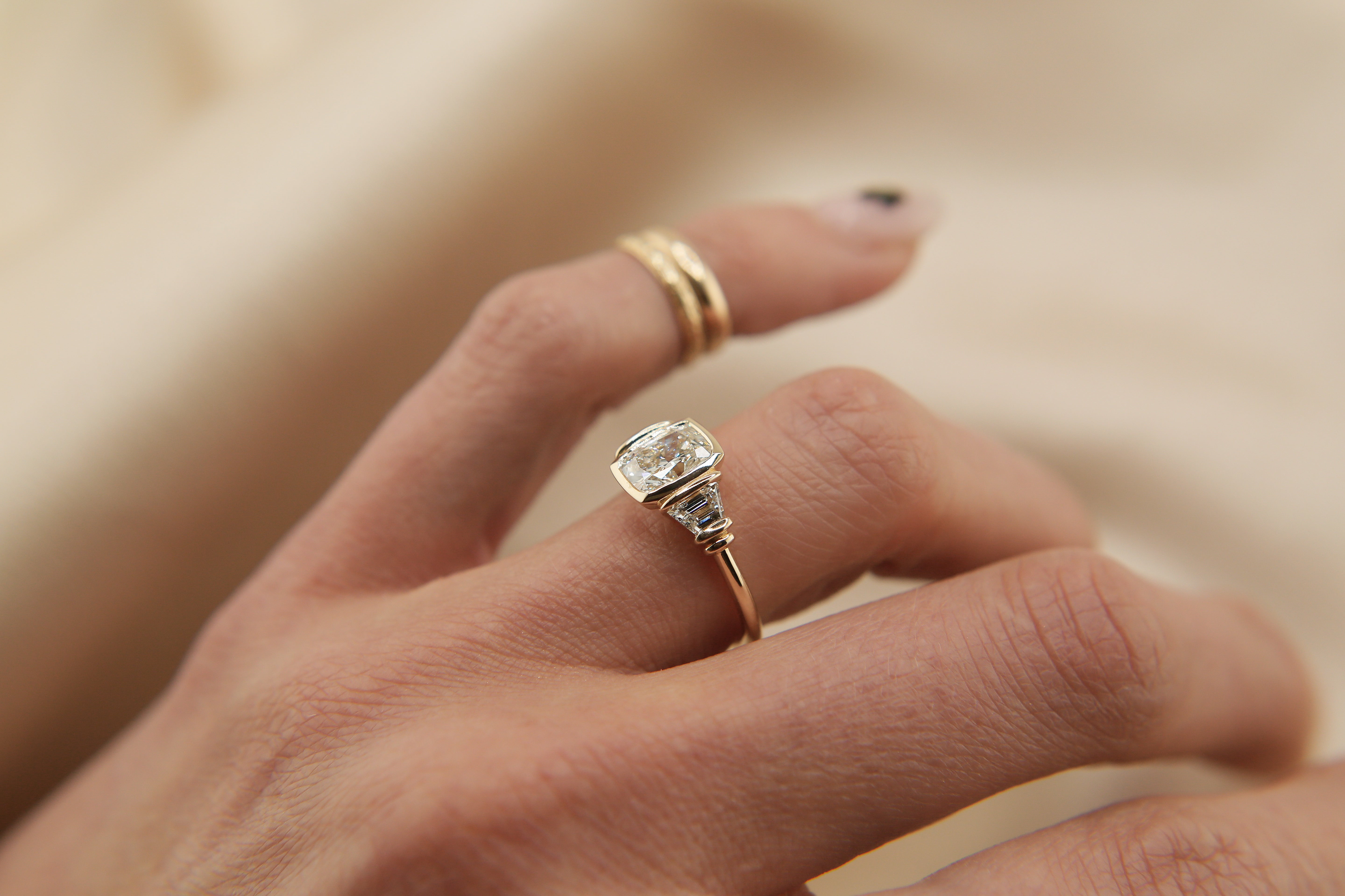 low profile cushion cut bezel set diamond three stone engagement ring, tab set trapezoid side stones on hand