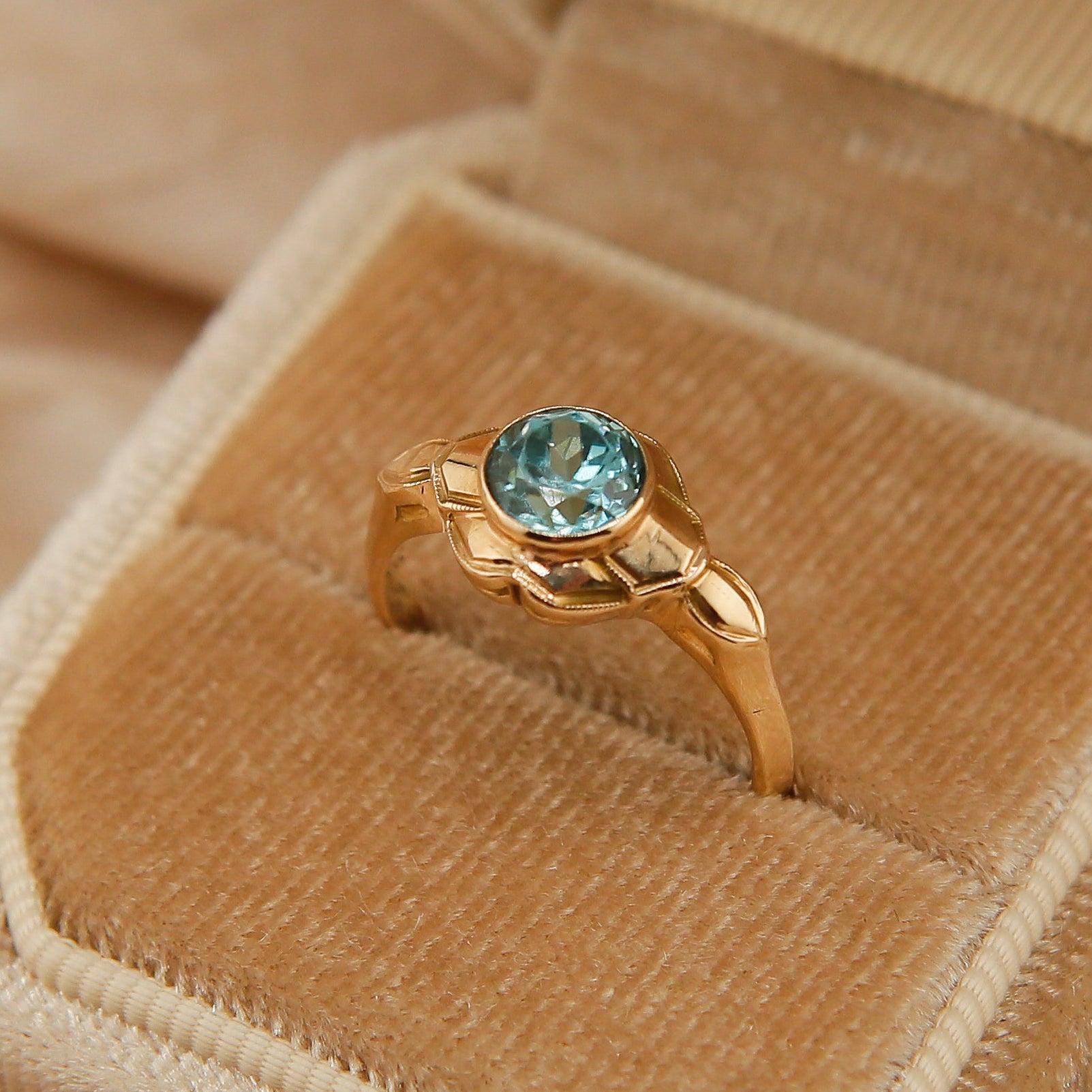 Gold ring with a blue gemstone in an open brown velvet box on a beige fabric background