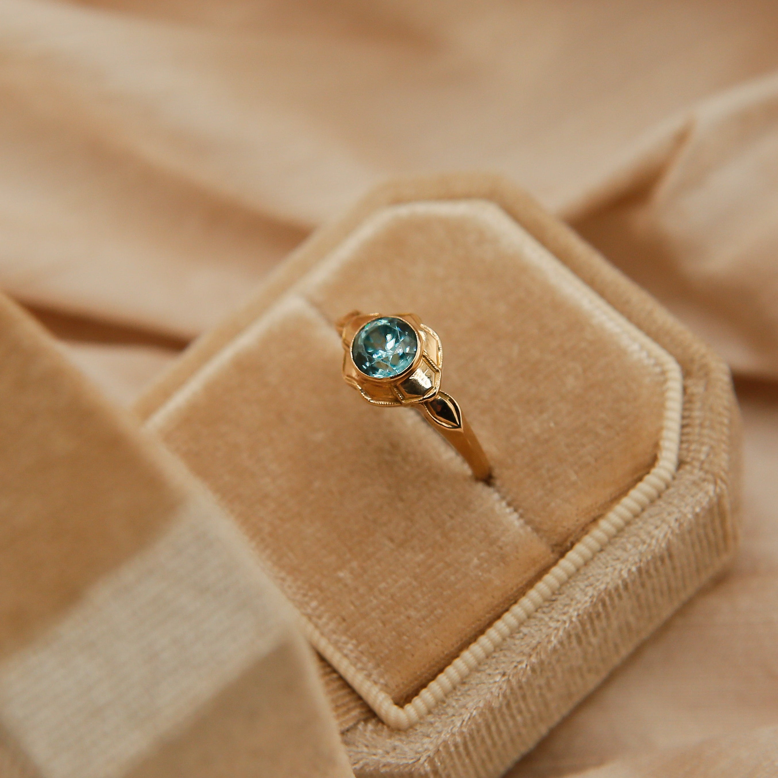 Gold ring with a green gemstone in a beige jewelry box on a beige fabric background
