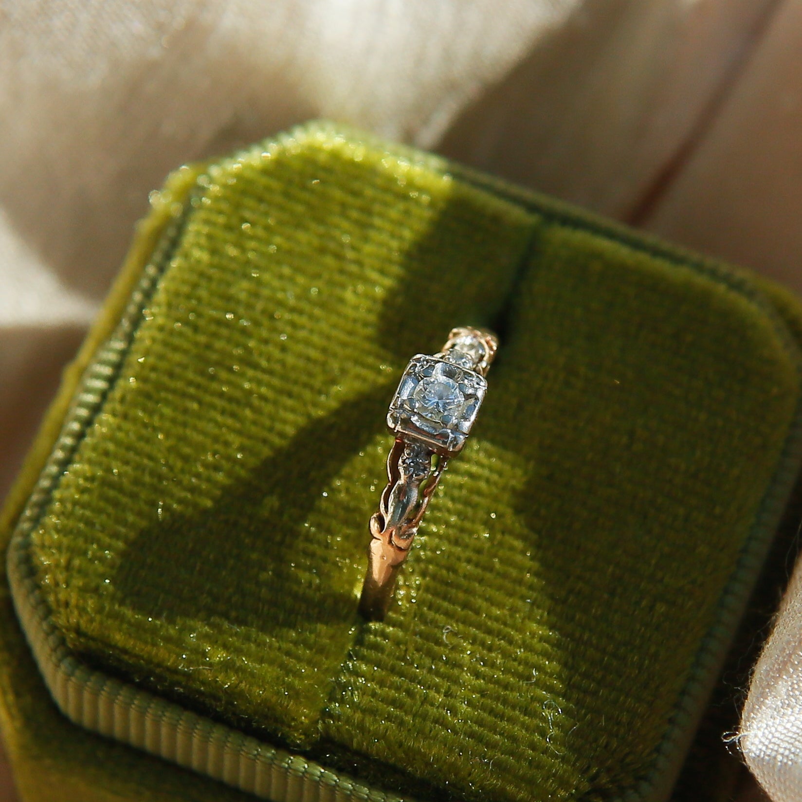 Gold ring with a diamond in a green velvet box on a light fabric background