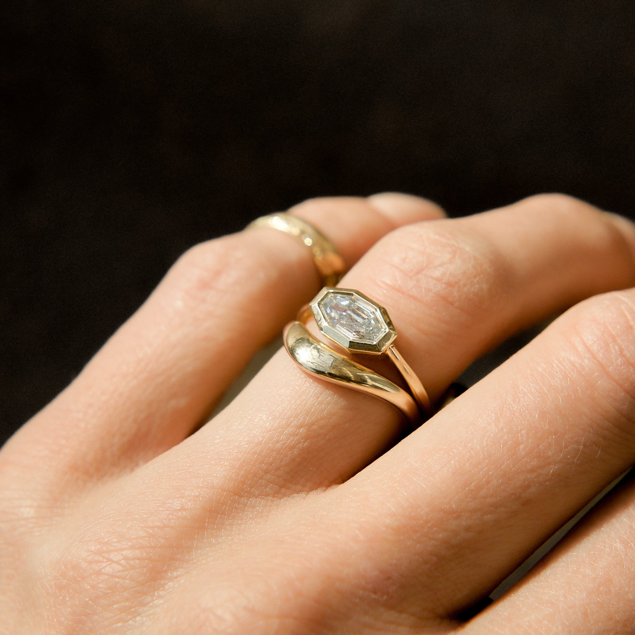 Close-up of a hand wearing two gold rings , our bezel set joey ring along with our contoured wave band. pairing them perfectly together.
