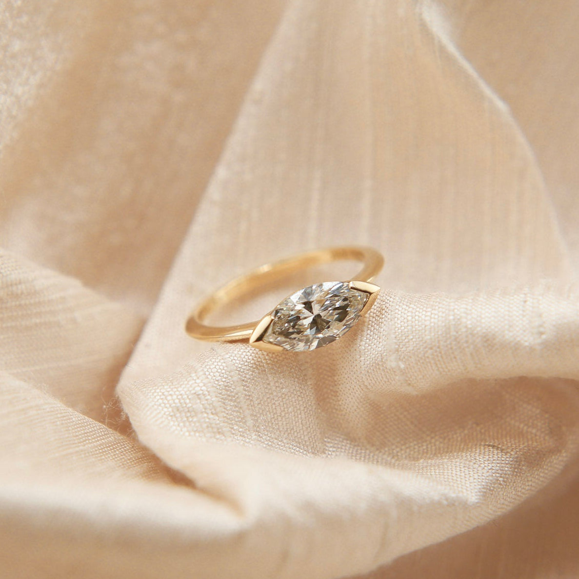 Gold ring with a diamond on a soft beige fabric background
