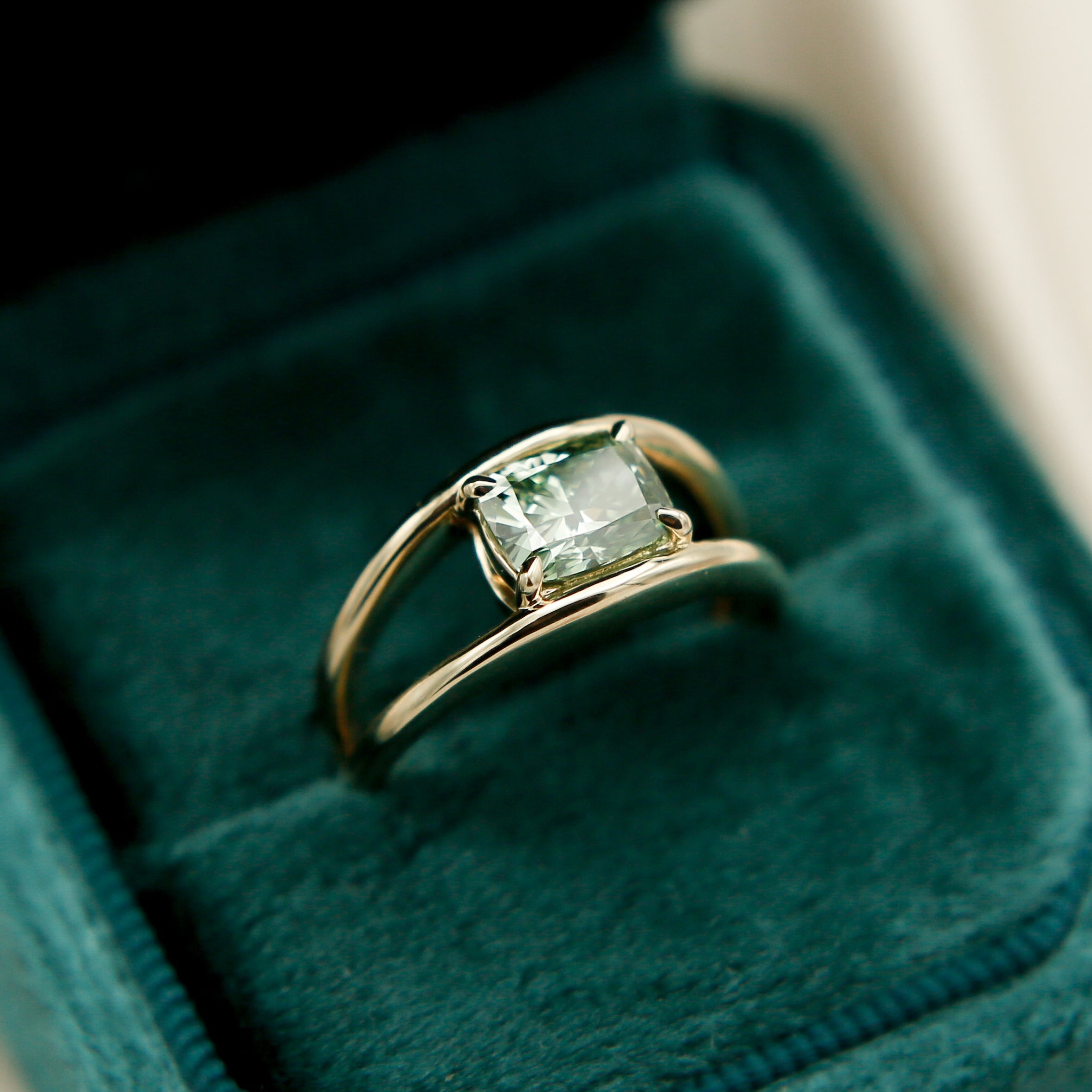 Gold ring with a green diamond gemstone in a green velvet box