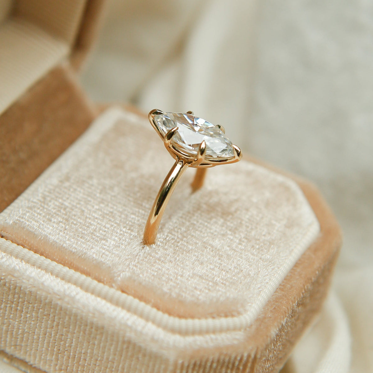 Gold ring with a diamond in a beige jewelry box on a soft beige fabric background