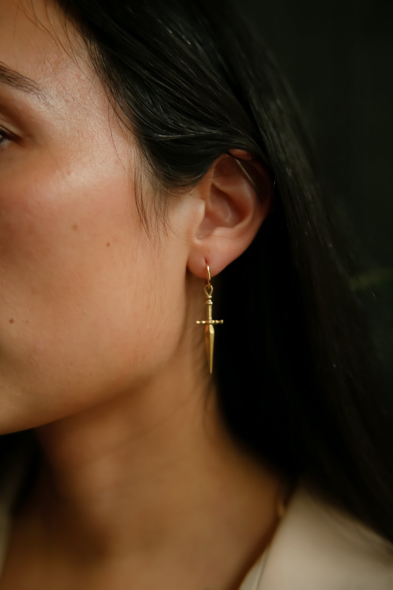 Model wearing brass hoop earring with sword hanging down