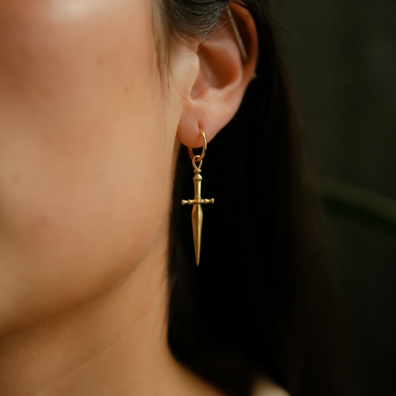 model wearing brass hoop earring with sword dangling down.