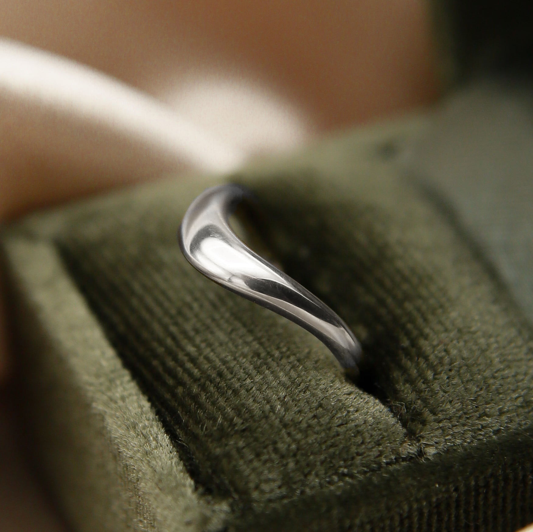 A wave style wedding band in white gold, displayed on a green velvet box.