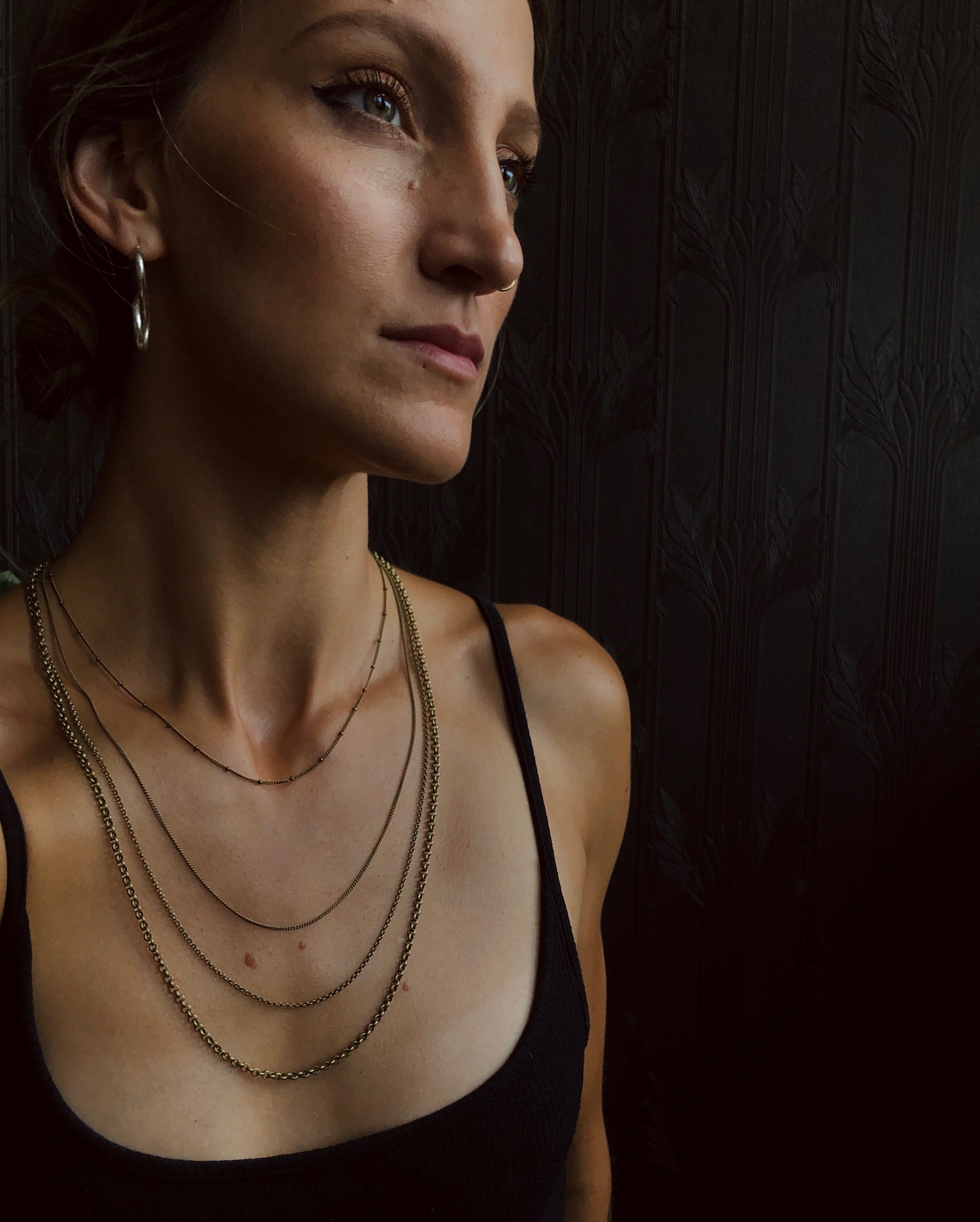 model wearing four brass chains of varying sizes and styles