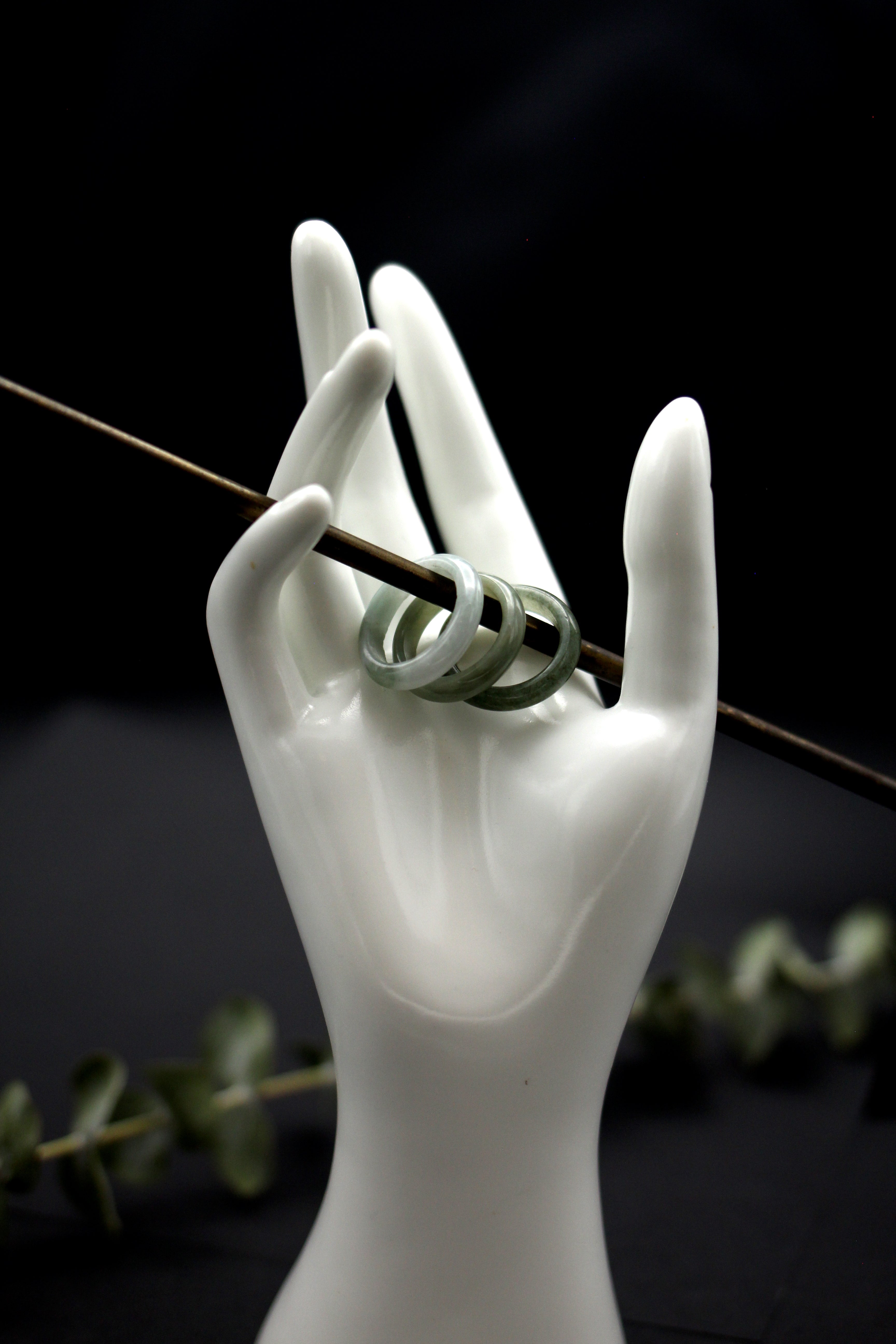 Three jade rings stacked on a stick held by a hand statue. lightest on the left, darkest on the right.