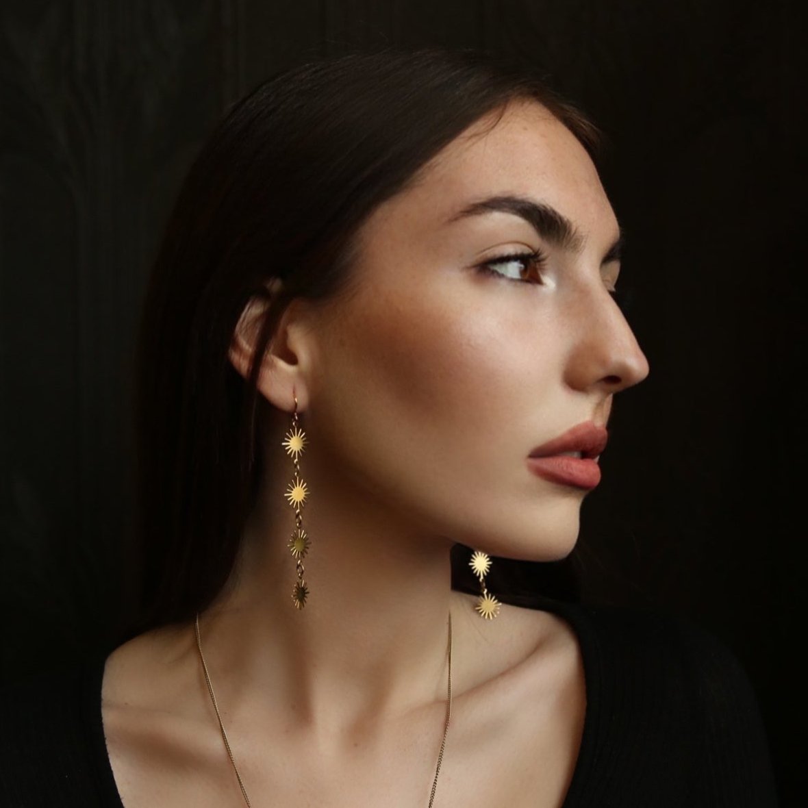 model wearing brass dangle earrings with four sun shaped pendants dropping