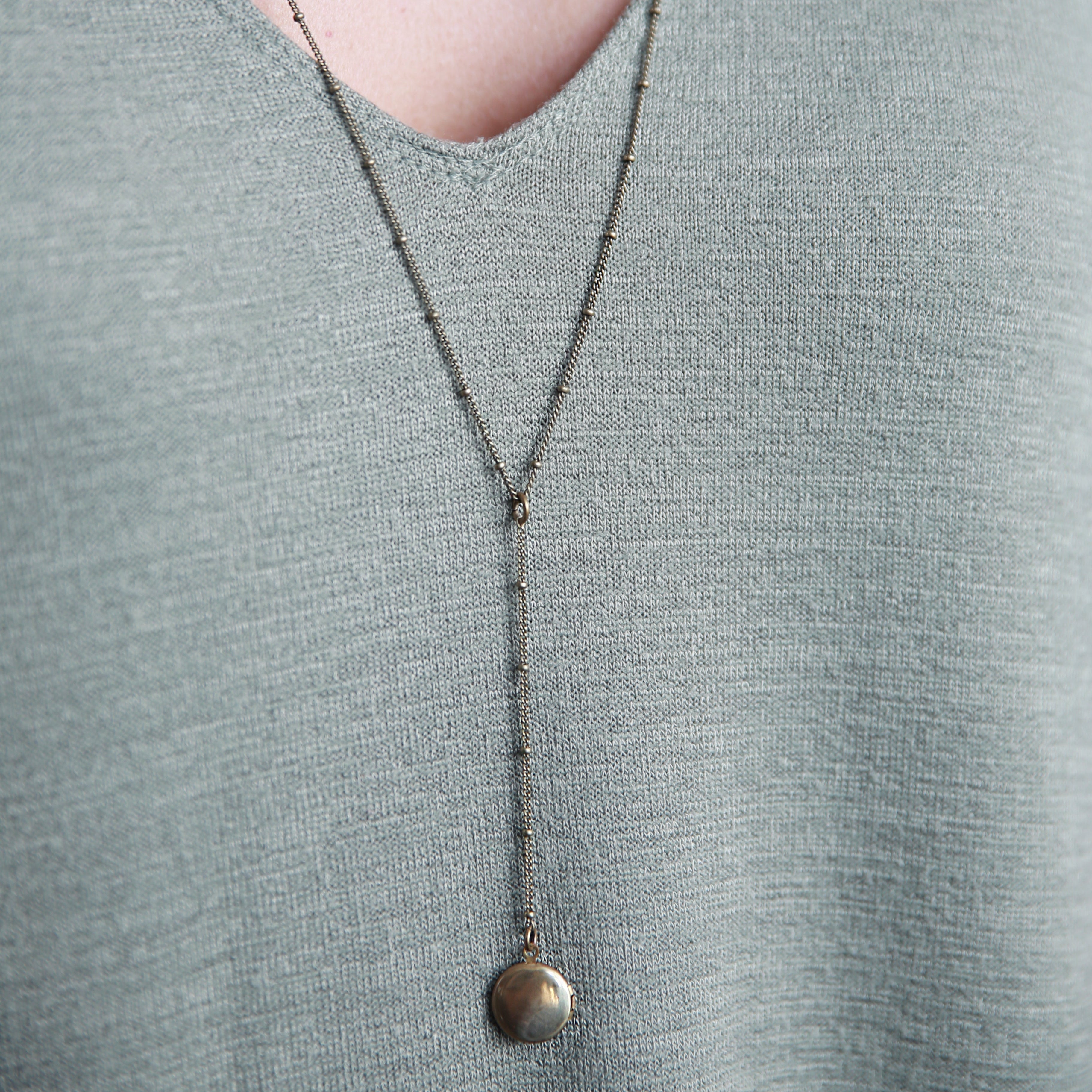 CIVAL Collective's "Vie" rosary style necklace on model that is 24 inches long and has a 2 inch drop with little brass locket at the end.