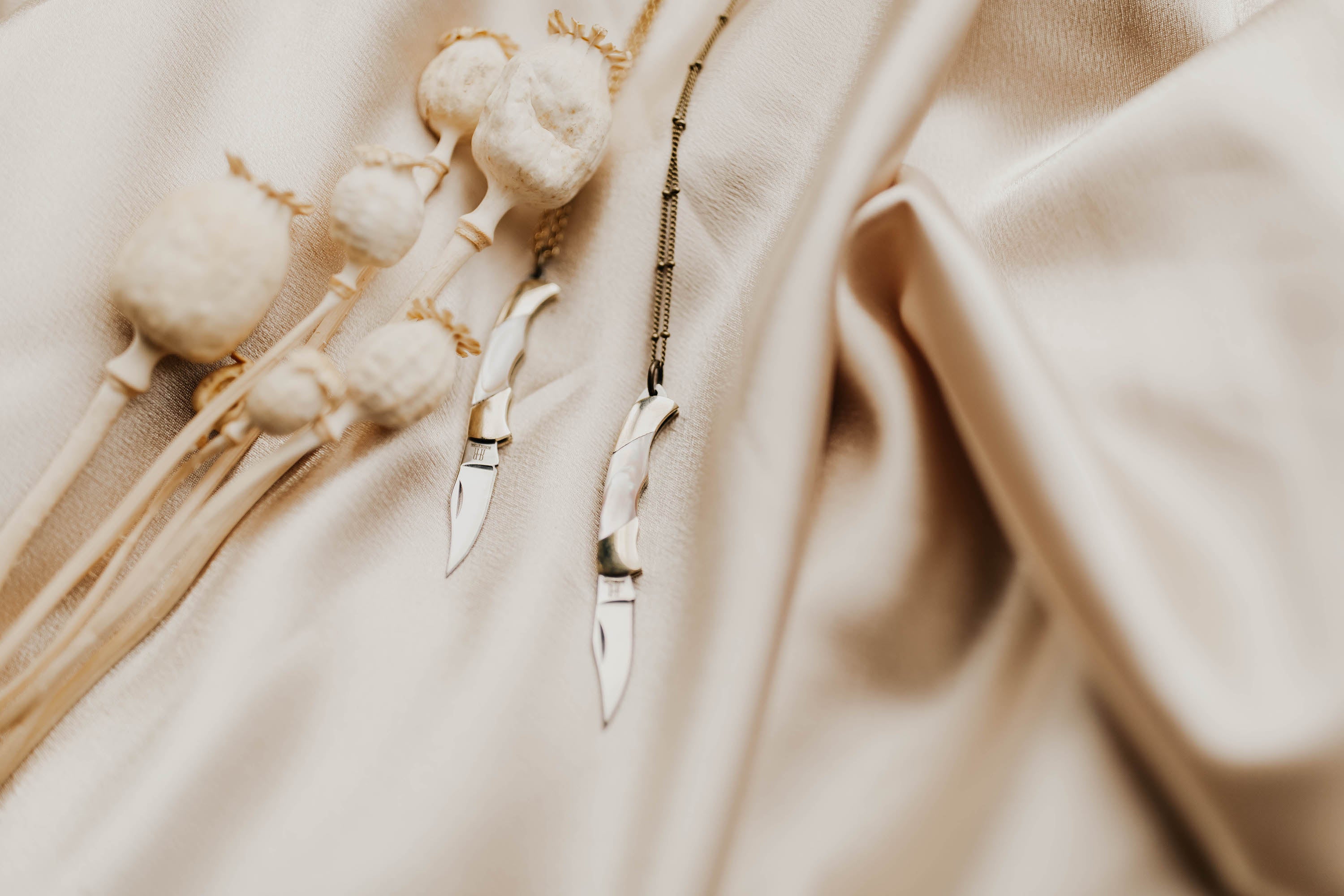 Two small pocket knife necklaces on brass satellite chains laid on creme fabric