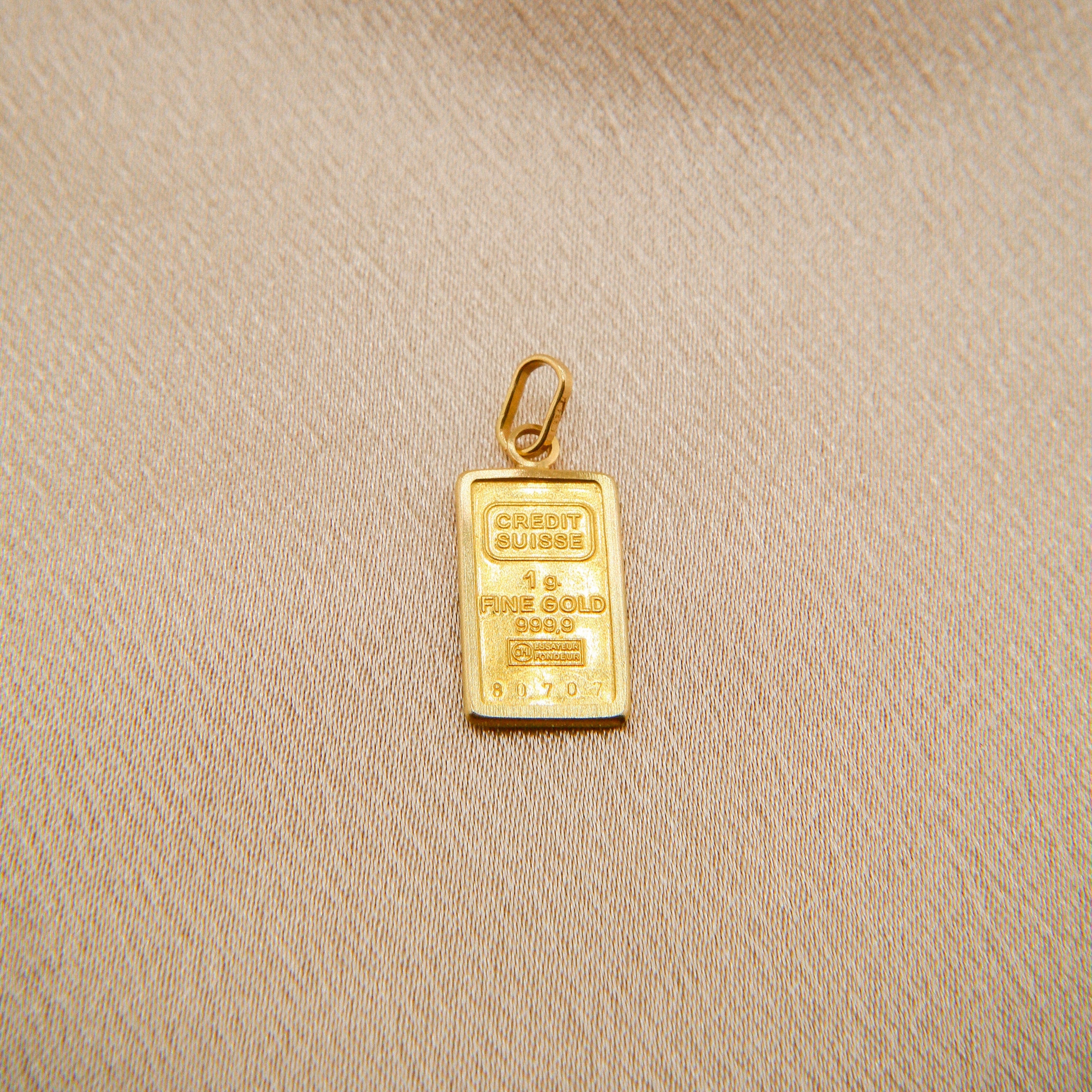 Gold bar pendant on a beige fabric background