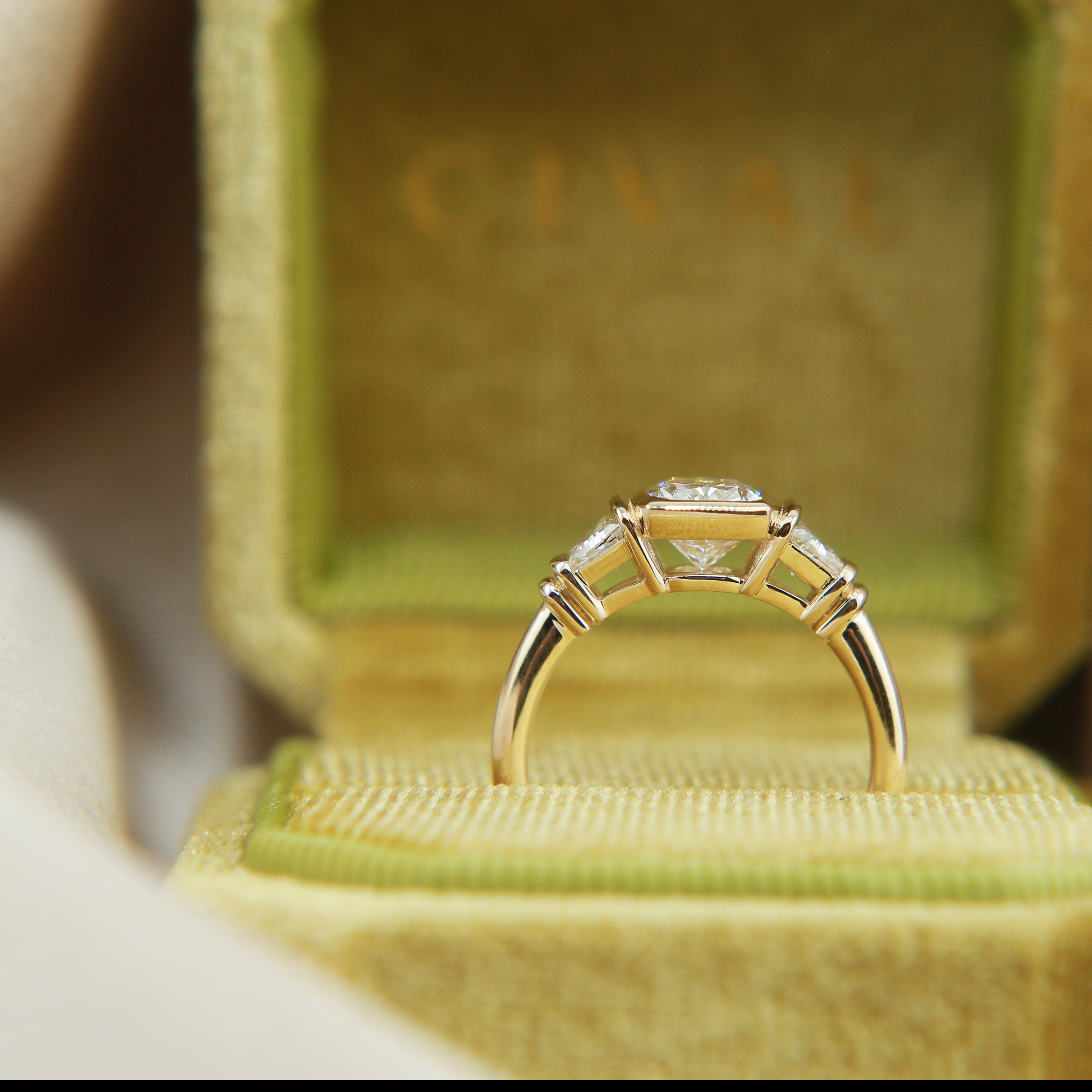 Cushion cut diamond three stone engagement, tab set trapezoid side stones in a velvet box. 