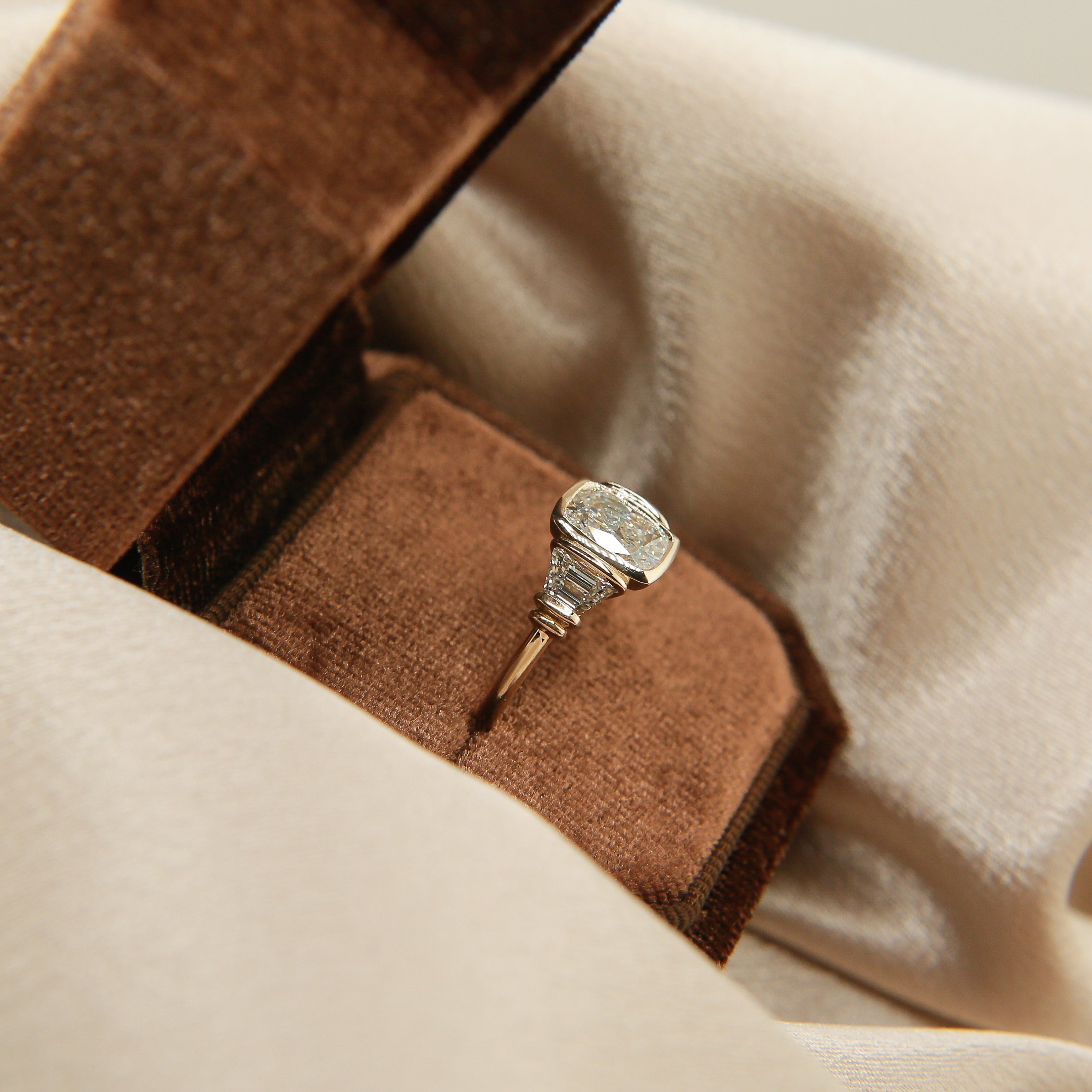 Cushion cut diamond three stone engagement ring, tab set trapezoid side stones in a velvet box. 