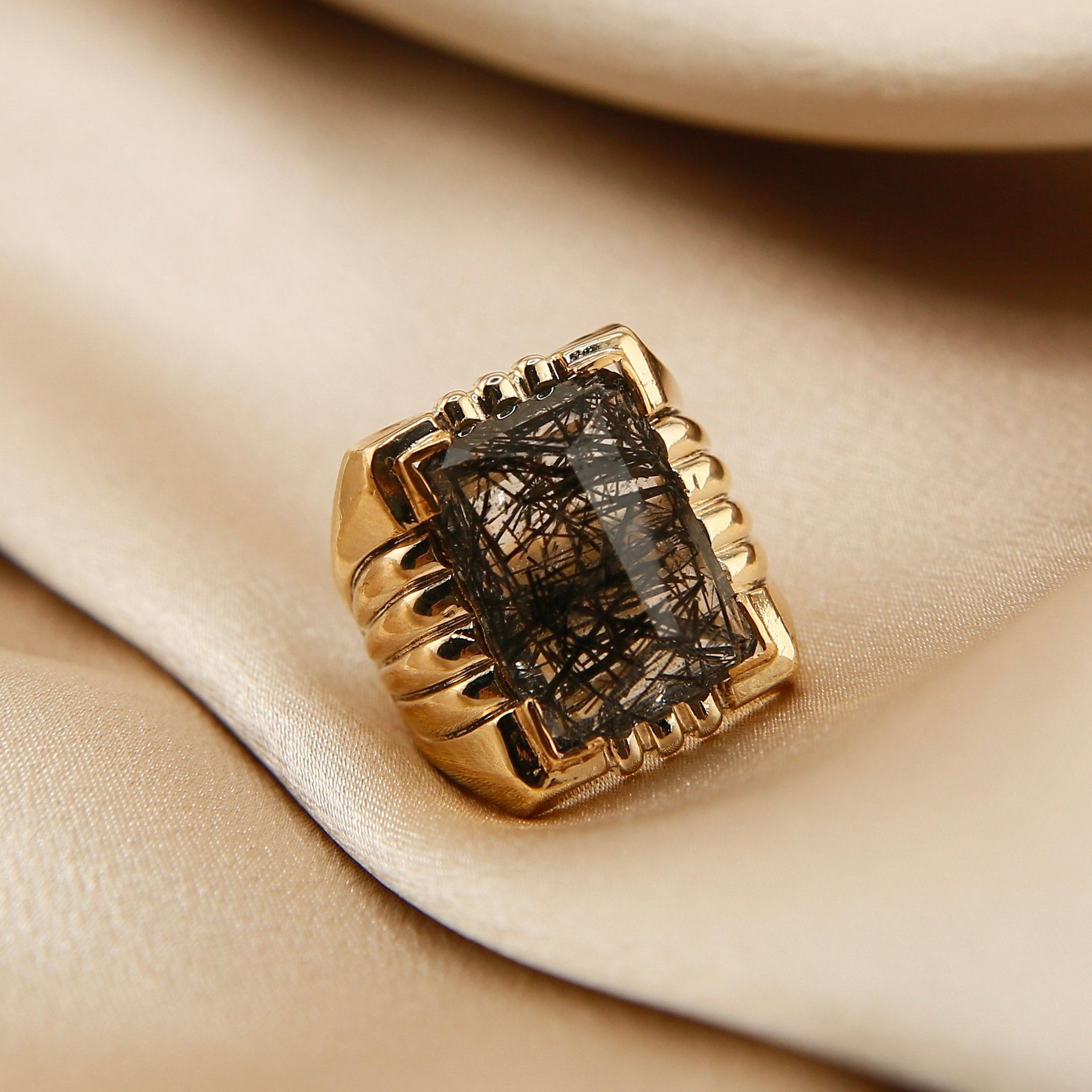 Gold ring with a dark gemstone on beige fabric