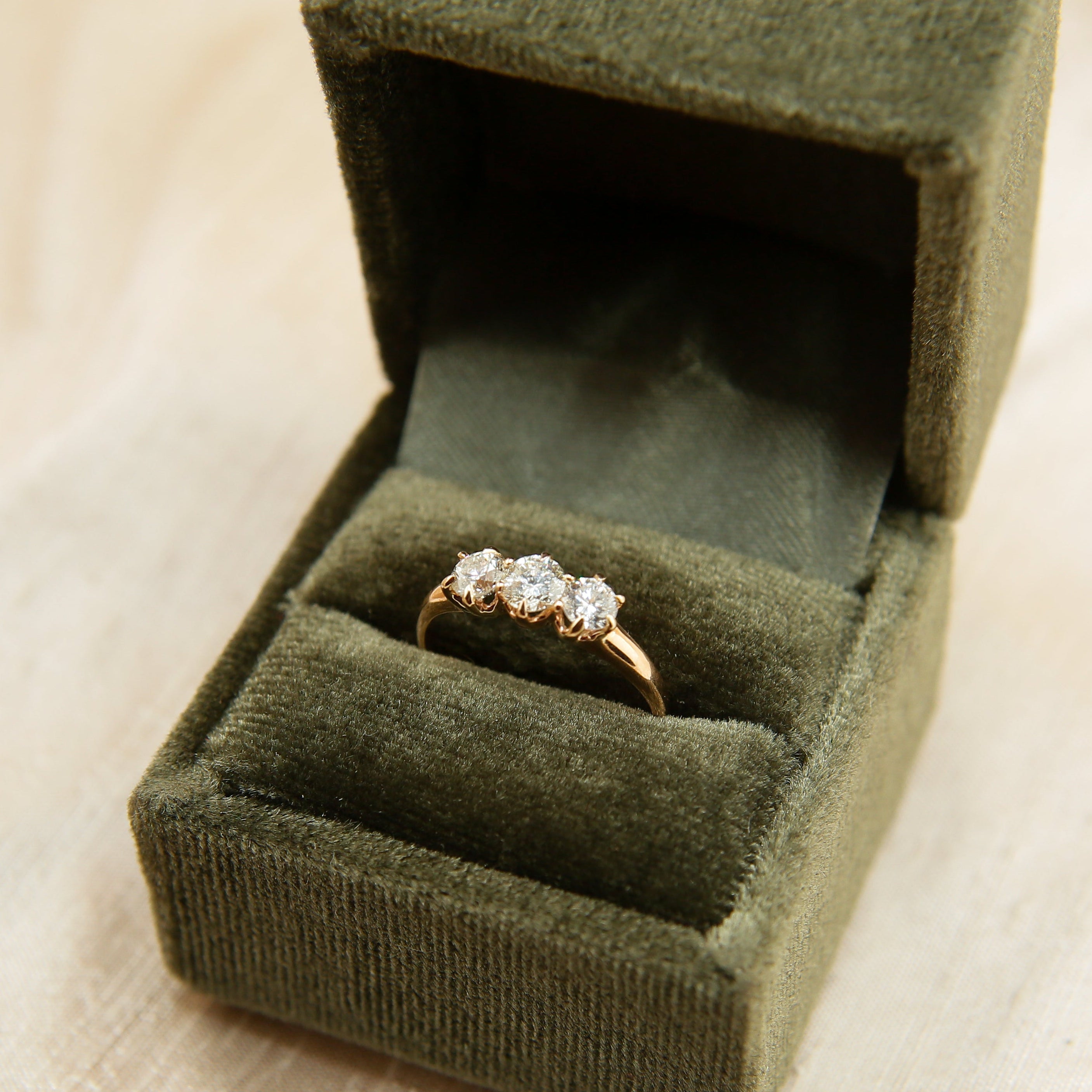 Gold ring with diamonds in a green velvet box on a beige fabric background