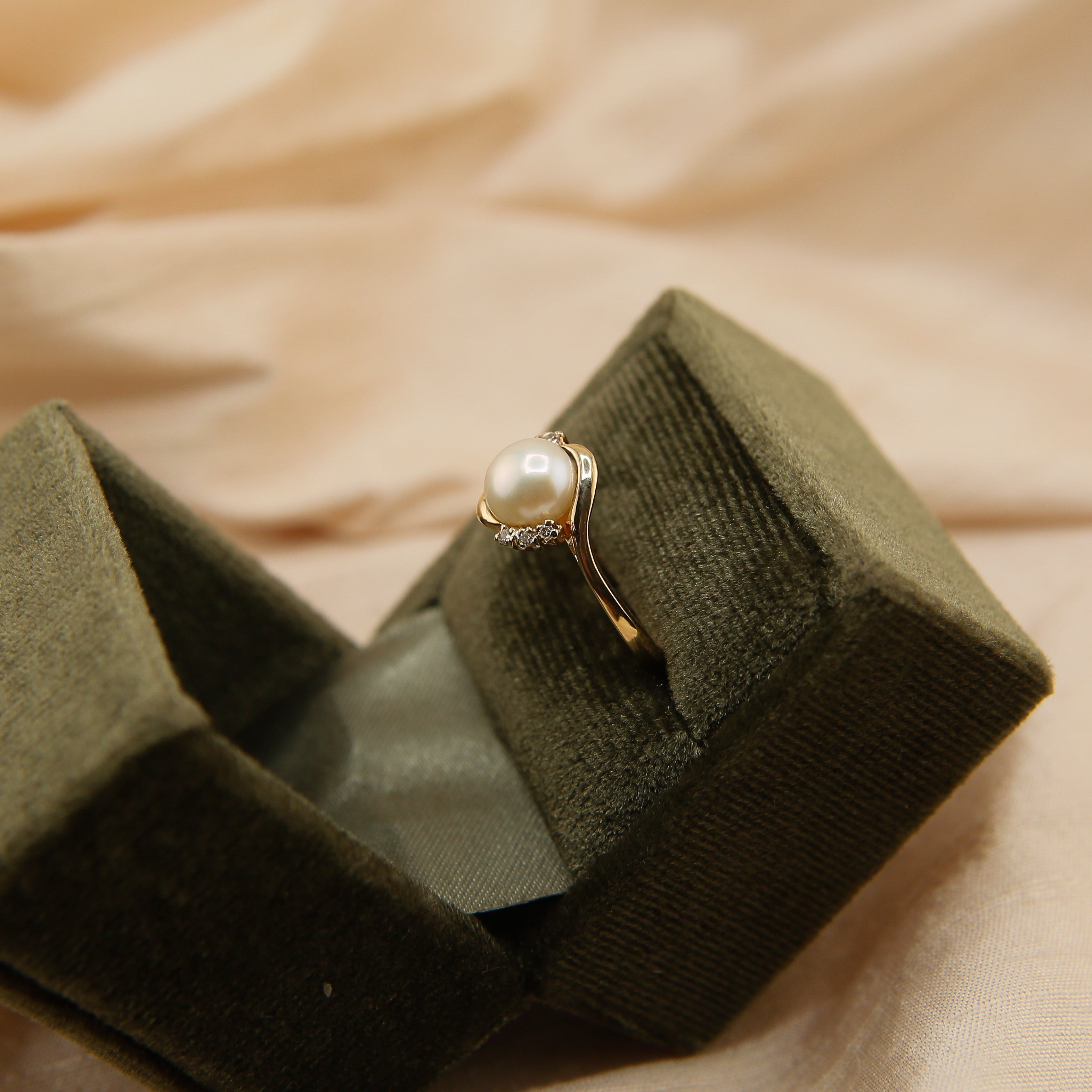 pearl ring in a green velvet box on a beige fabric background