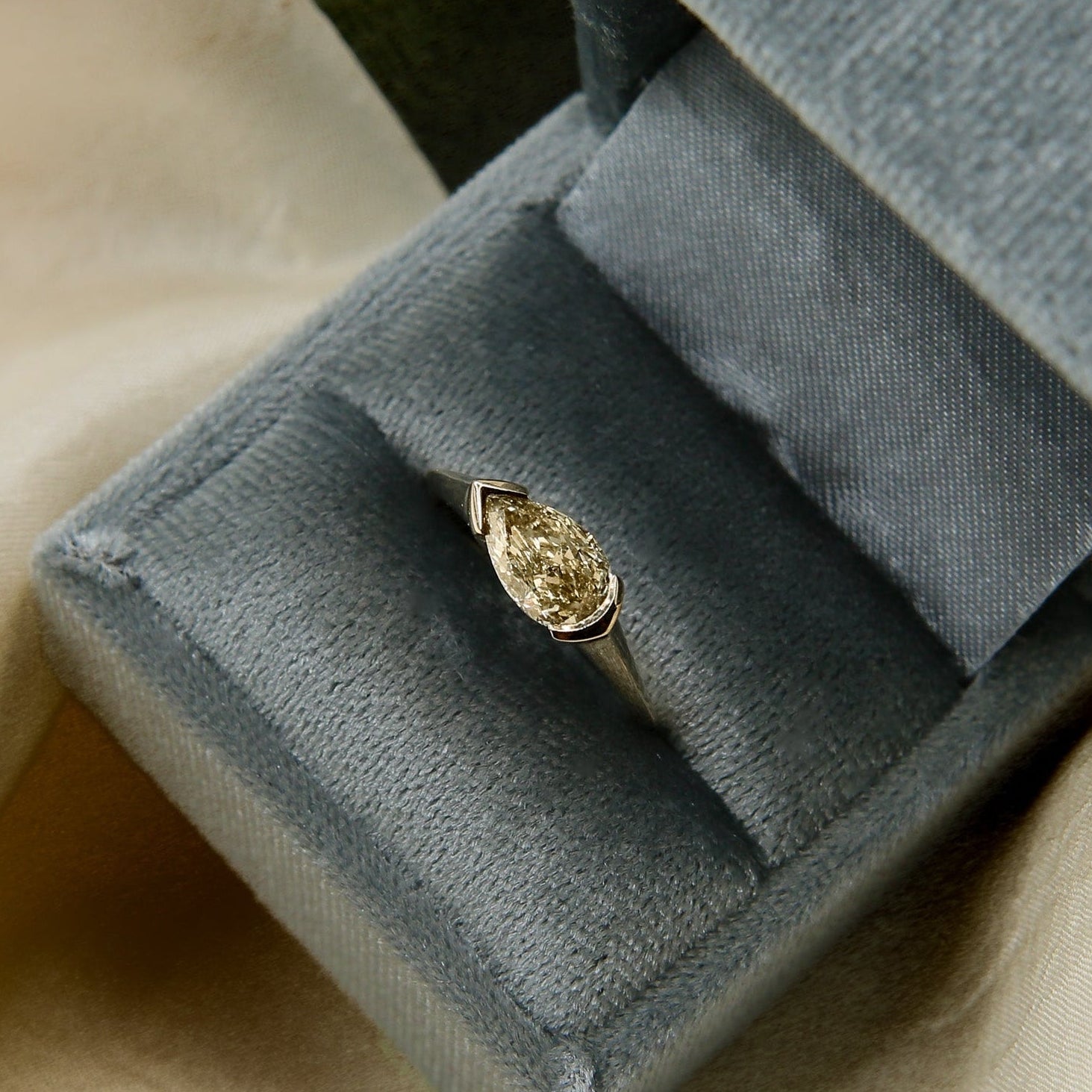 Gold ring with a pear-shaped diamond in a gray velvet box on beige fabric