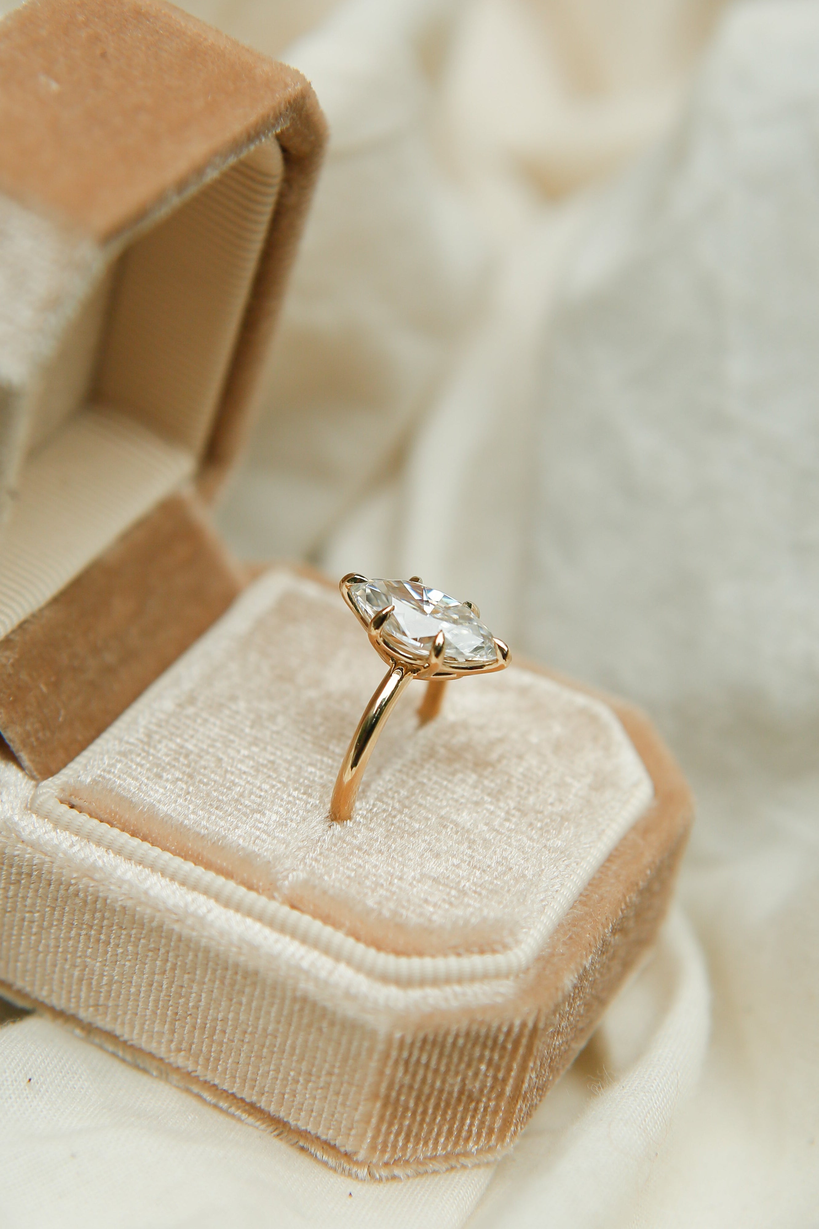 Gold ring with a diamond in a beige jewelry box on a soft beige fabric background