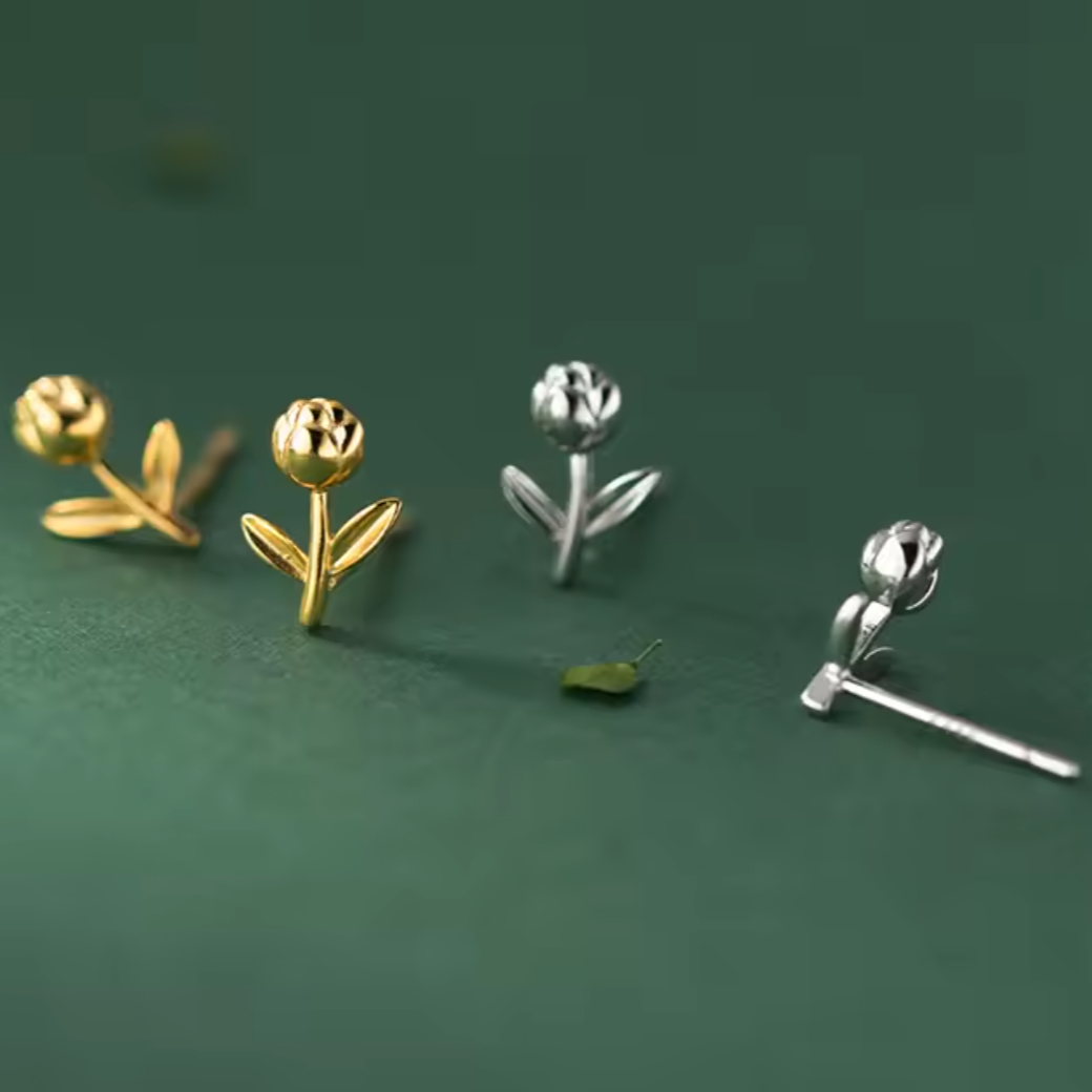 Two pairs of flower-shaped earrings, one gold and one silver, on a green background.