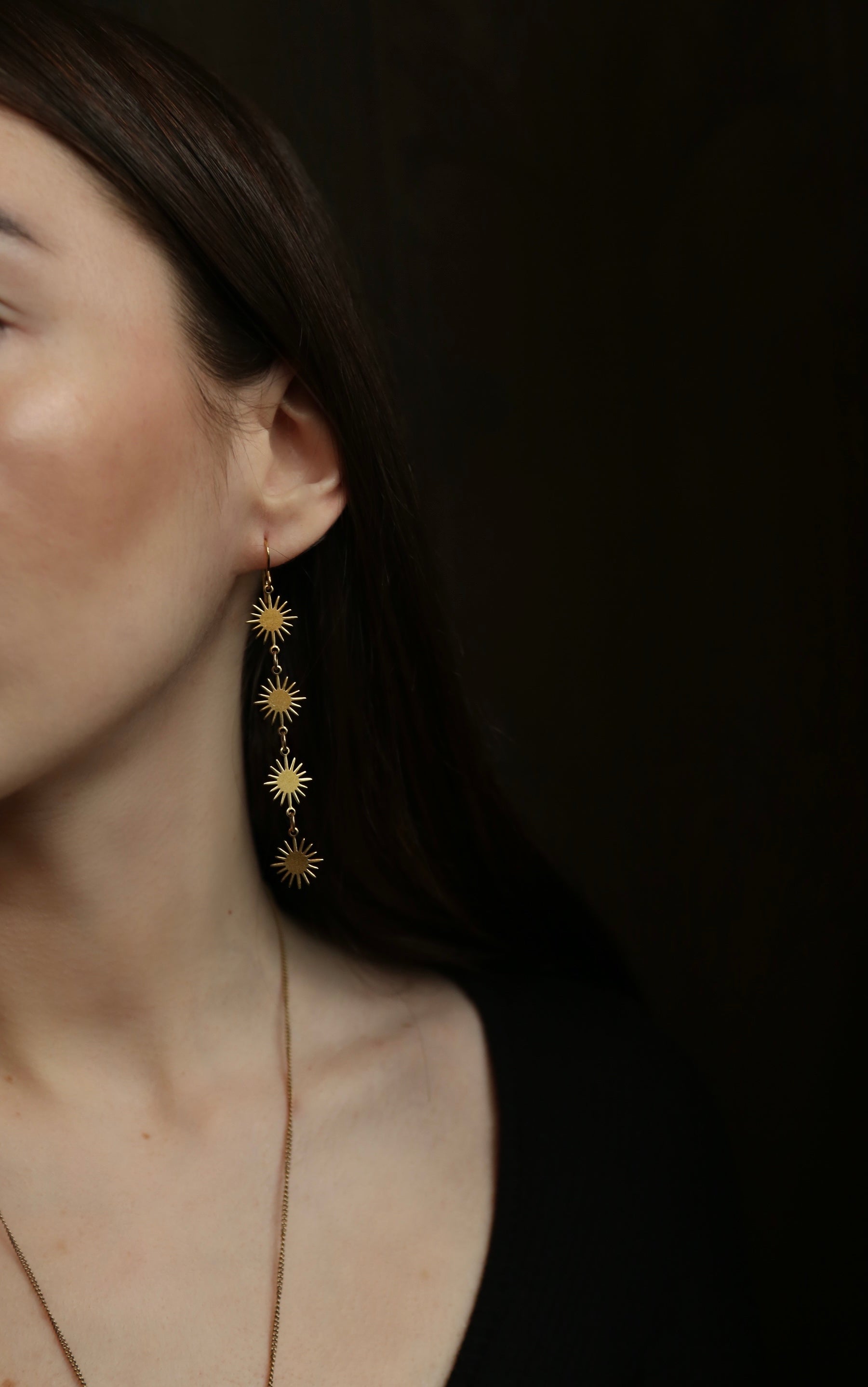 model wearing brass dangle earrings with four sun shaped pendants dropping 