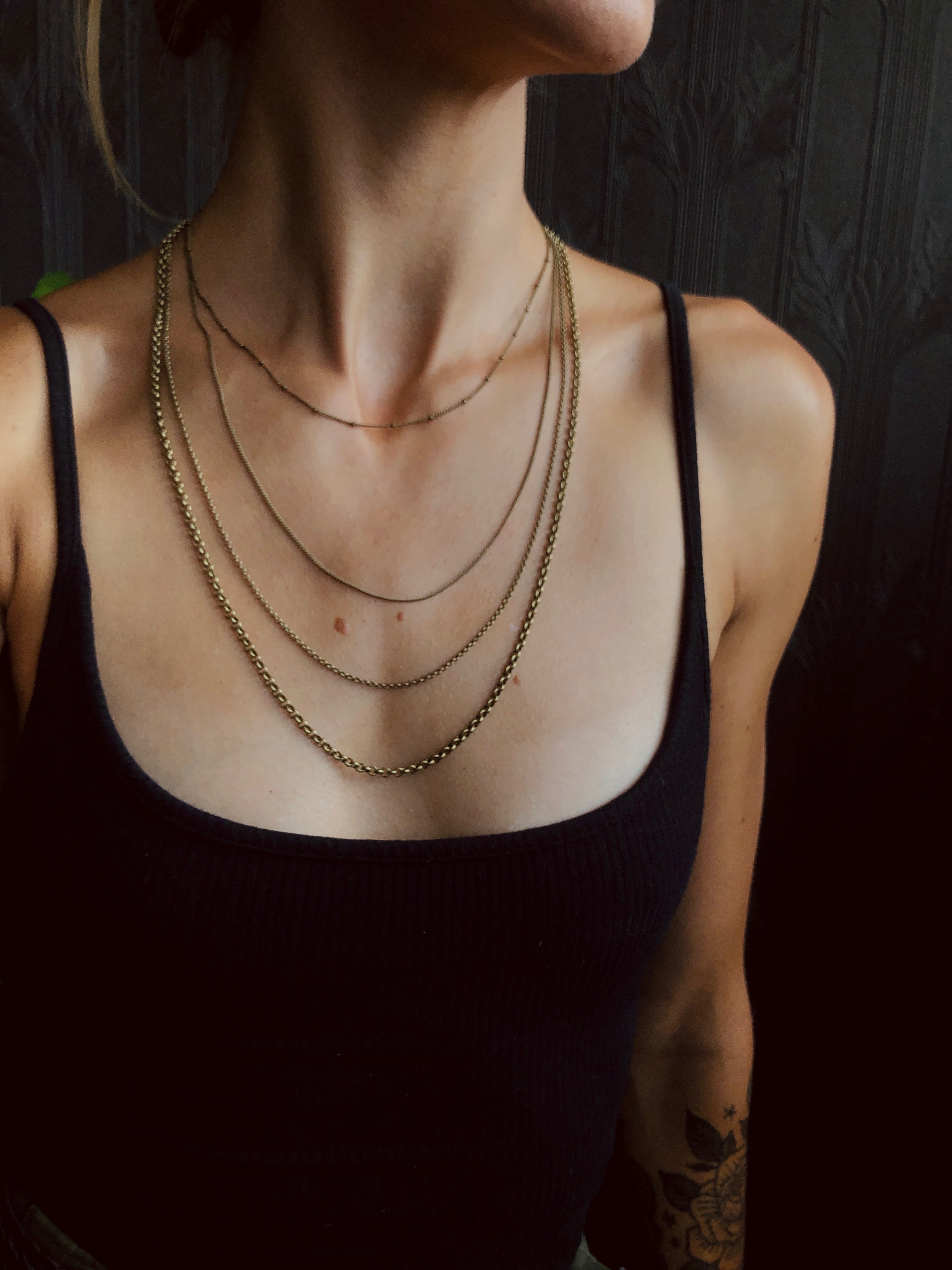 model wearing four brass chains of varying sizes and styles