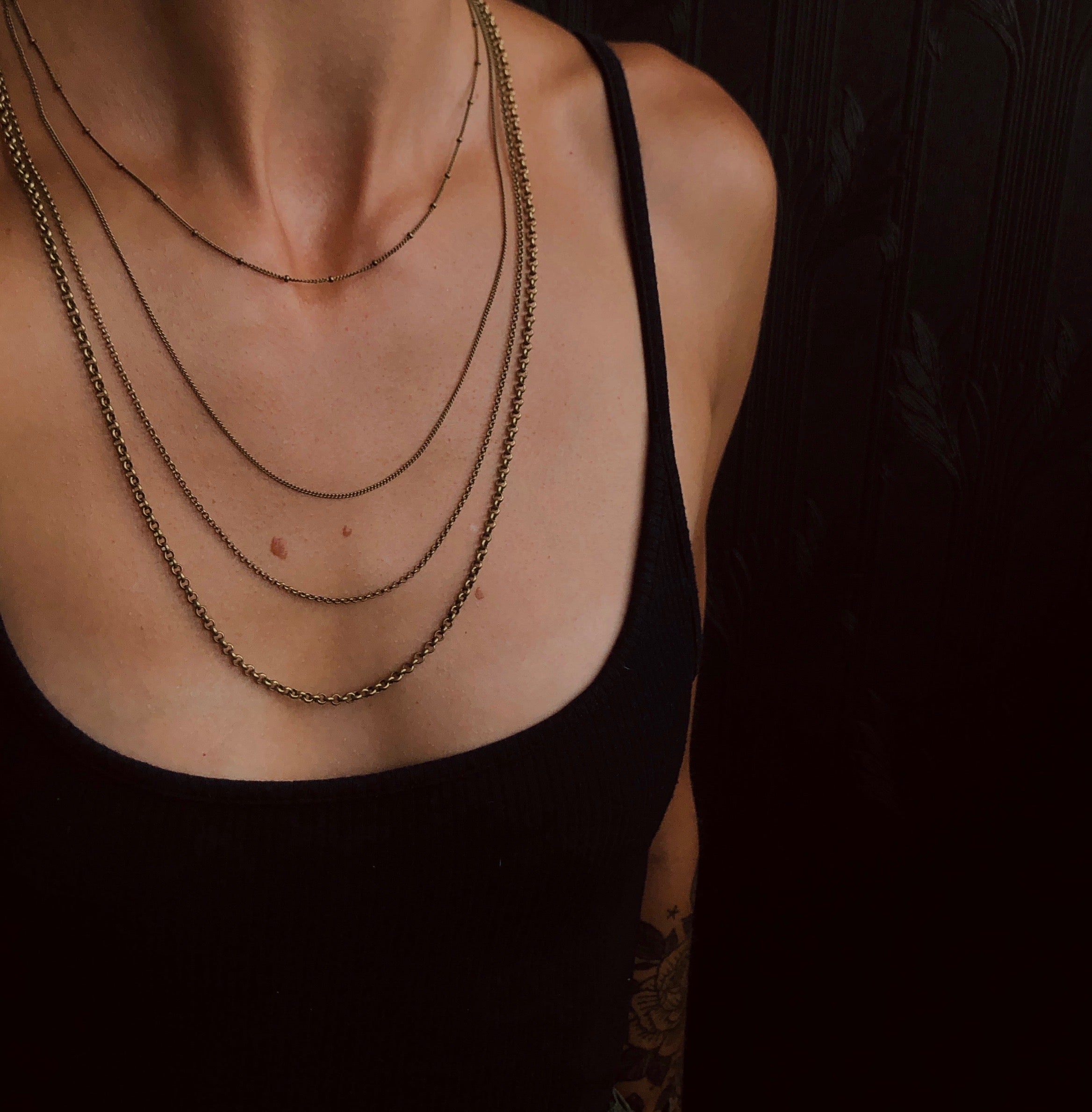 model wearing four brass chains of varying sizes and styles