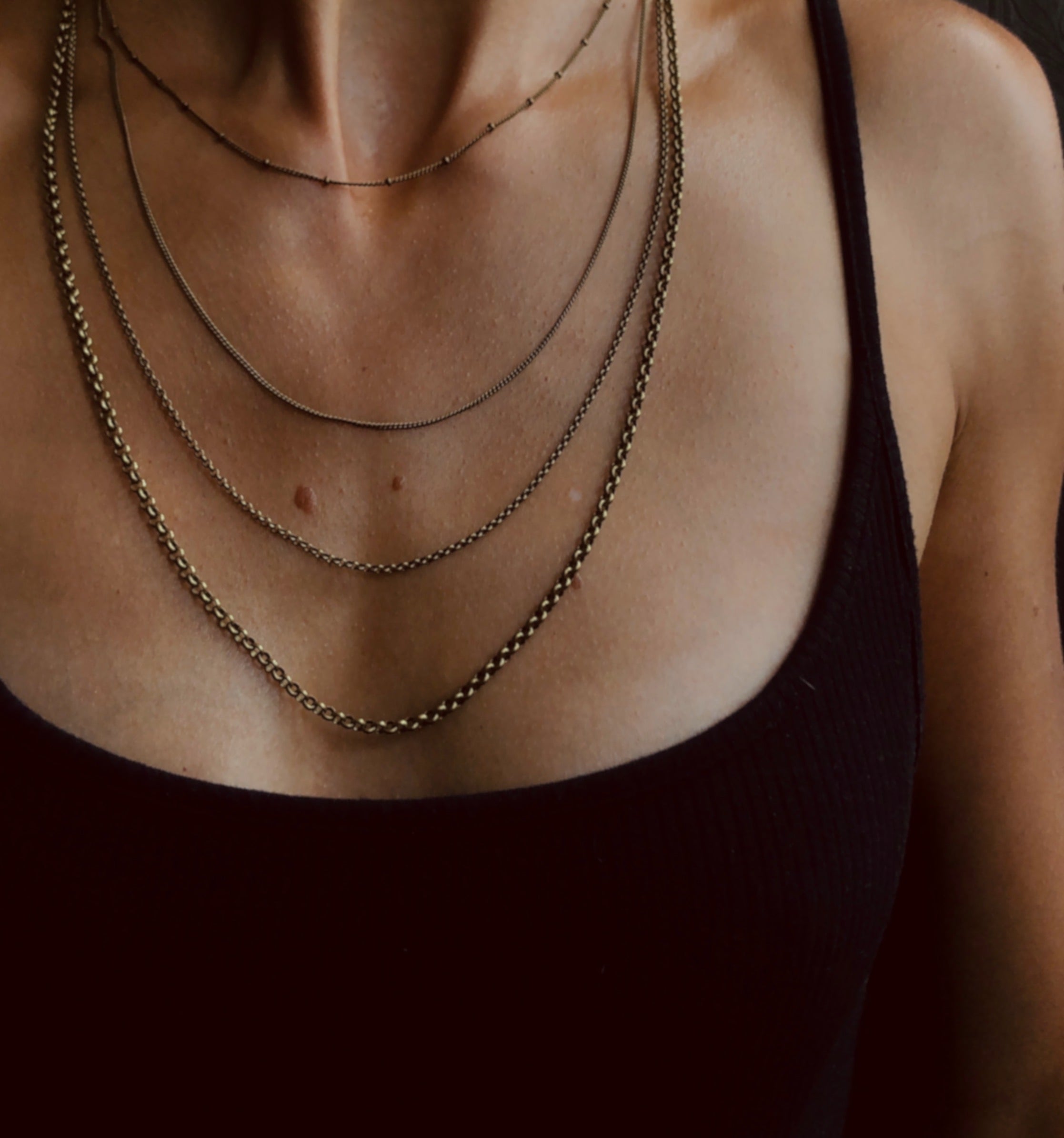 model wearing four brass chains of varying sizes and styles