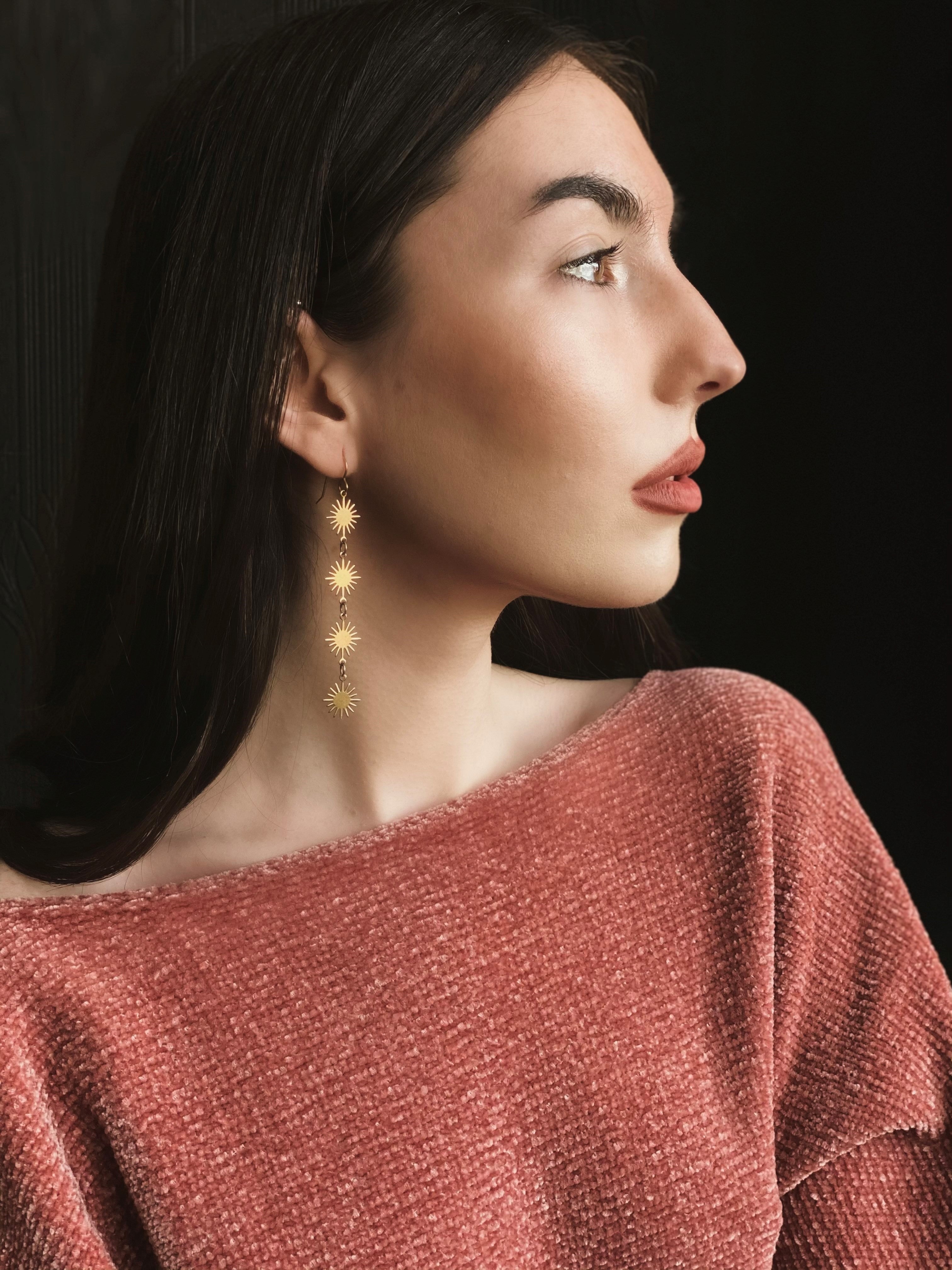 model wearing brass dangle earrings with four sun shaped pendants dropping 
