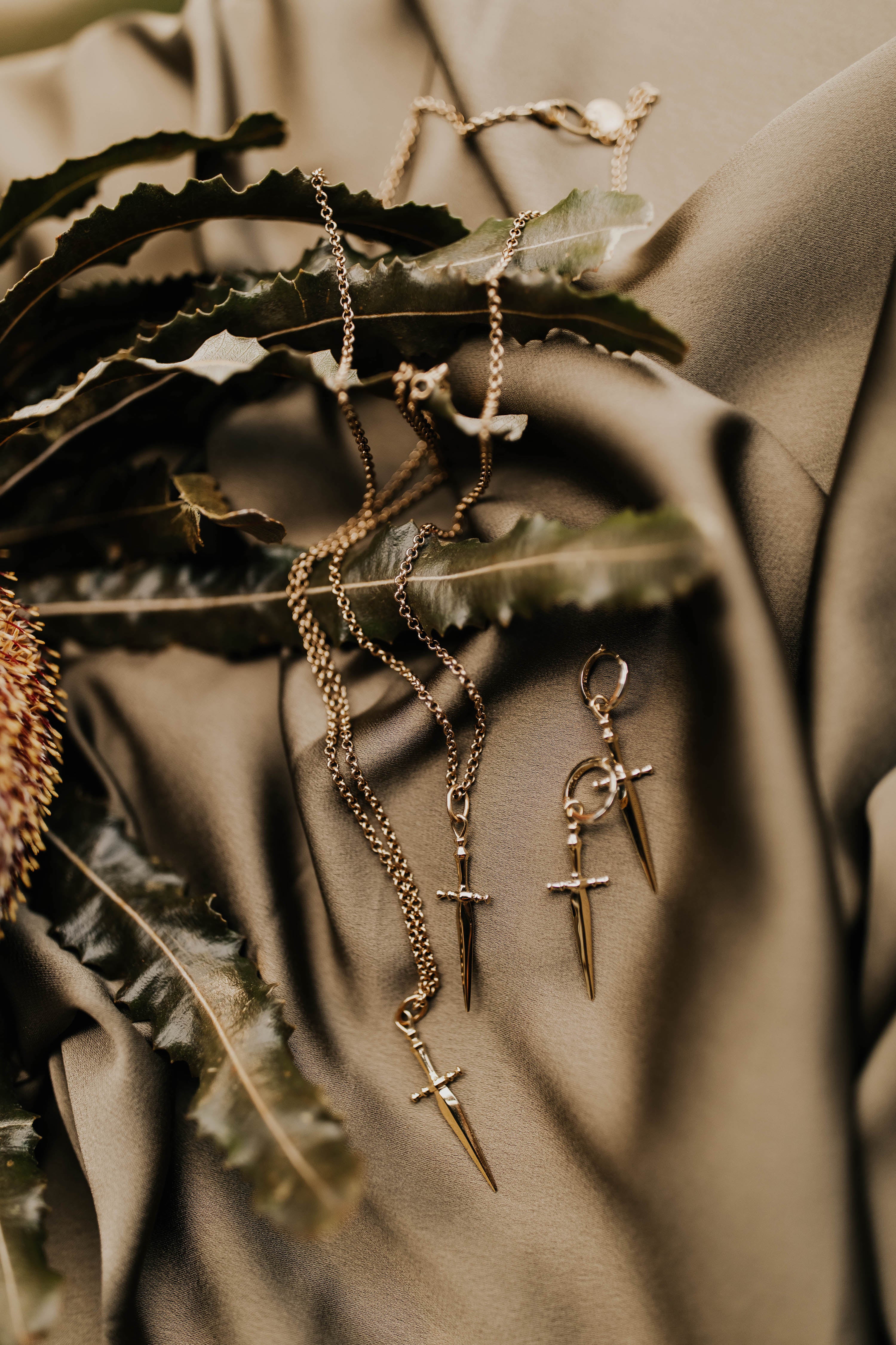Two brass hoop with swords earrings with swords next to two brass sword necklaces